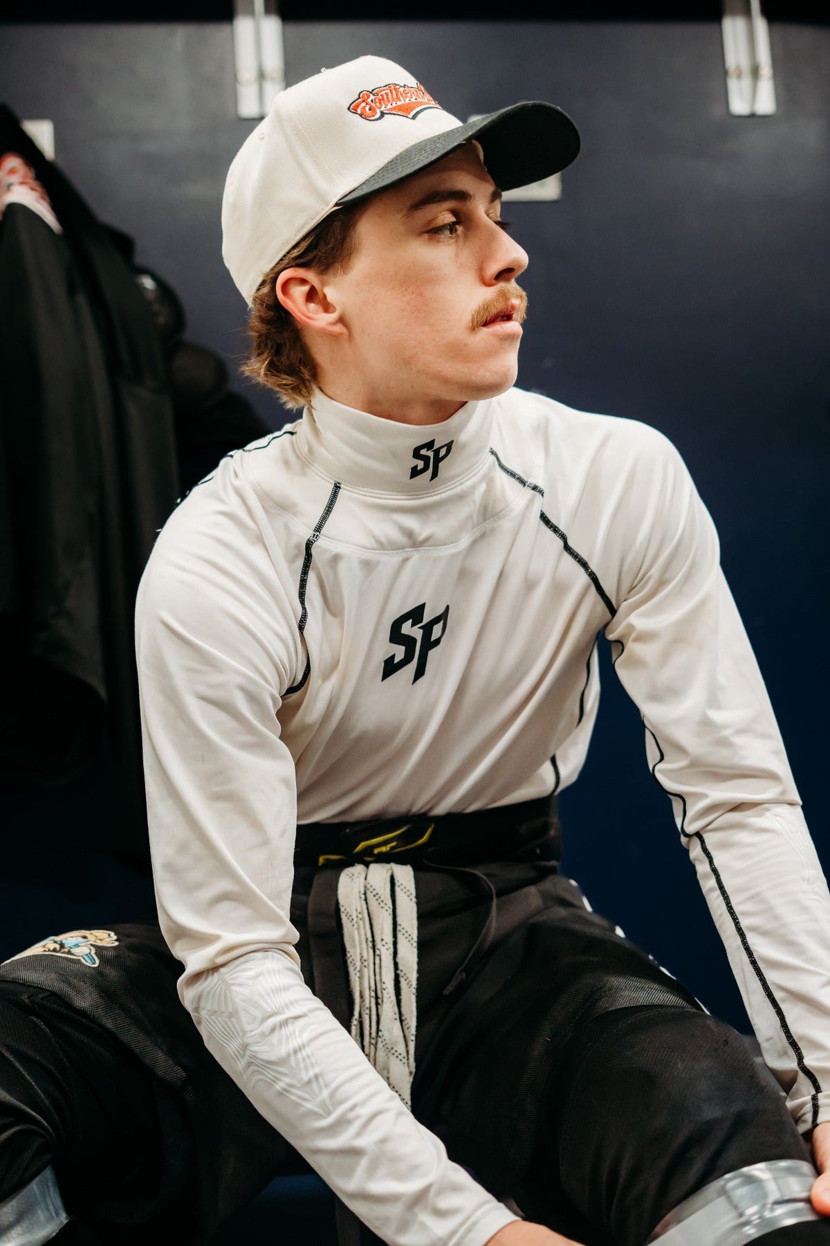 Side view of adult hockey player wearing Southern Puck white neck guard shirt in a locker room