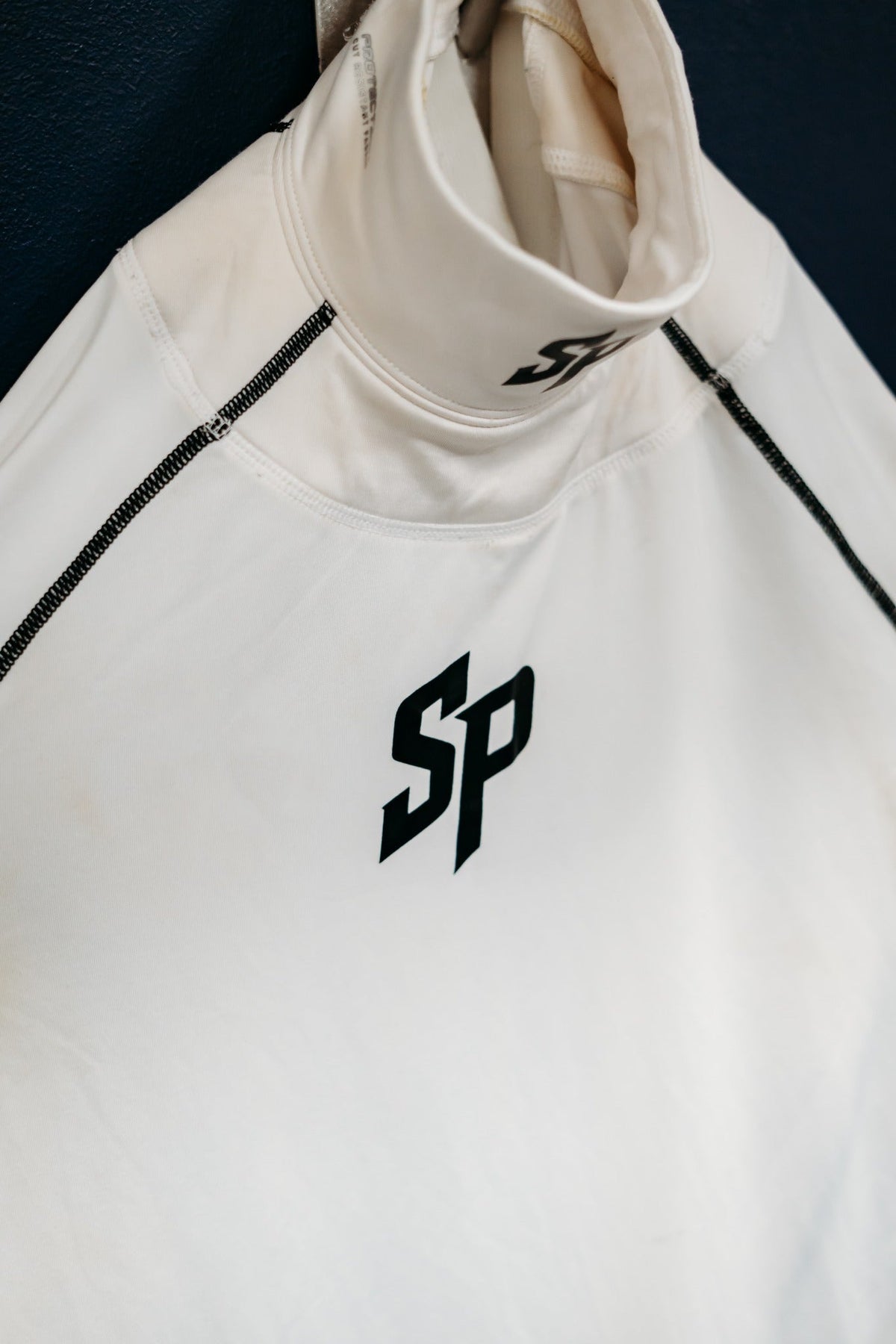 White Southern Puck neck guard performance shirt hanging in a locker room, adult version shown for Youth product design reference